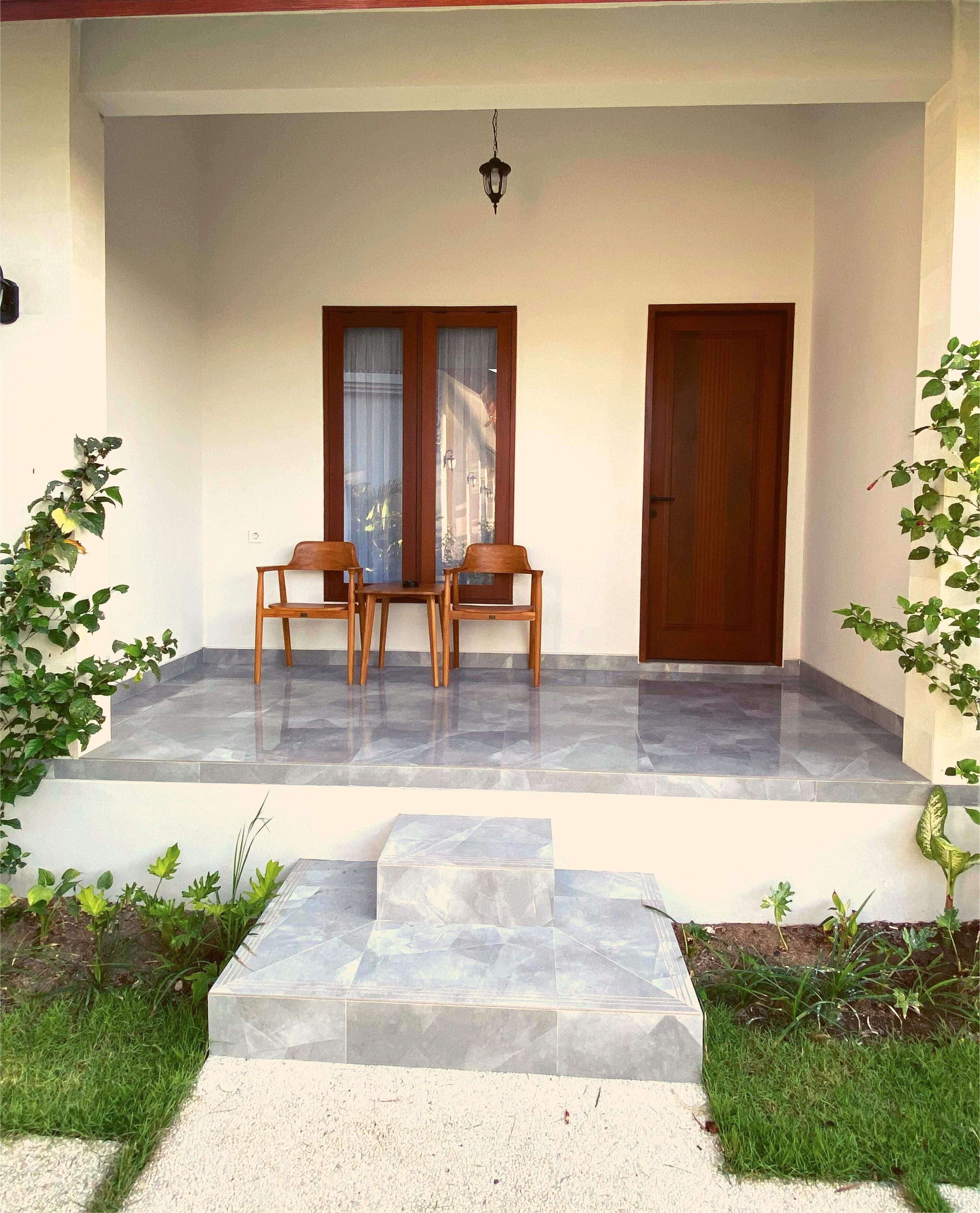 A covered outdoor seating area with two wooden chairs and a table, a door, and a hanging light fixture.