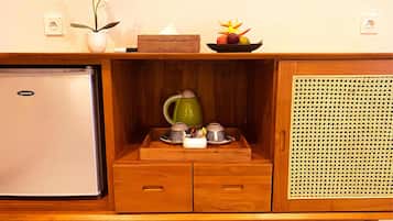 A compact kitchenette with a refrigerator, a tea set, and a wicker cabinet.