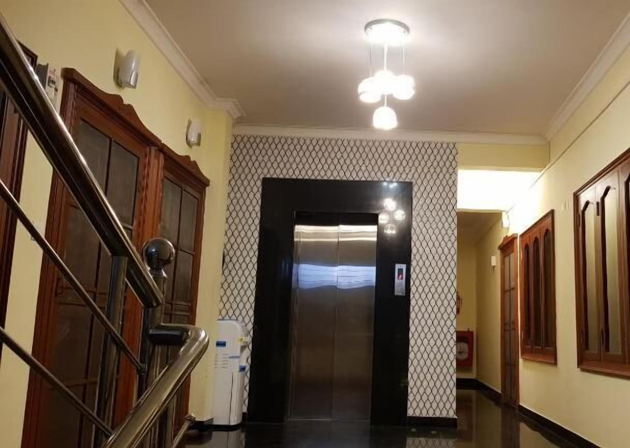 Un pasillo con un ascensor negro, una escalera con barandillas de madera y un revestimiento mural estampado.