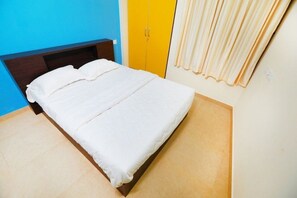 A bed with white bedding in a room with a blue wall and a yellow wardrobe.