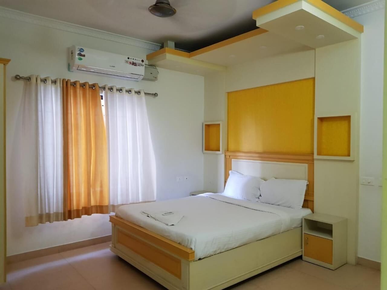 Une chambre à coucher comprenant un lit, des tables de chevet, une commode, un appareil de climatisation et une fenêtre avec des rideaux.