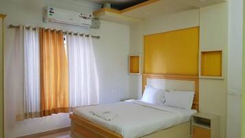Une chambre à coucher comprenant un lit, des tables de chevet, une commode, un appareil de climatisation et une fenêtre avec des rideaux.