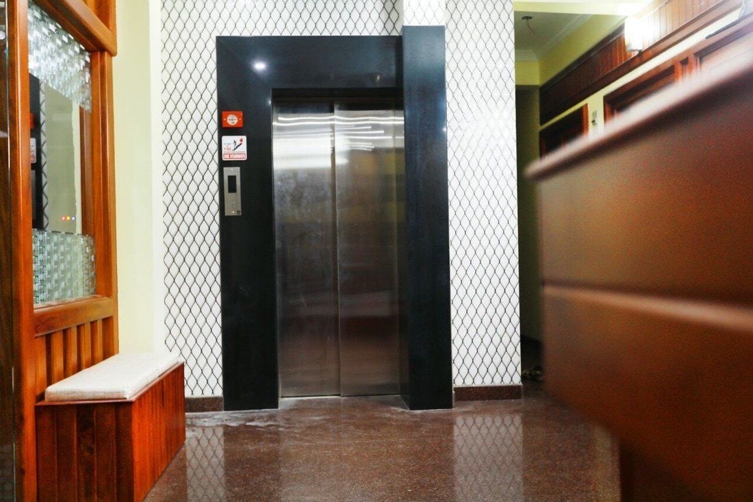 Un ascensor amb acabat metàl·lic, un senyal de seguretat i una banca de fusta a l'esquerra.