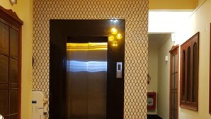 A hallway with a polished floor, a patterned wall, and a door leading to an elevator. - Shalom Residency (Kanayannur)