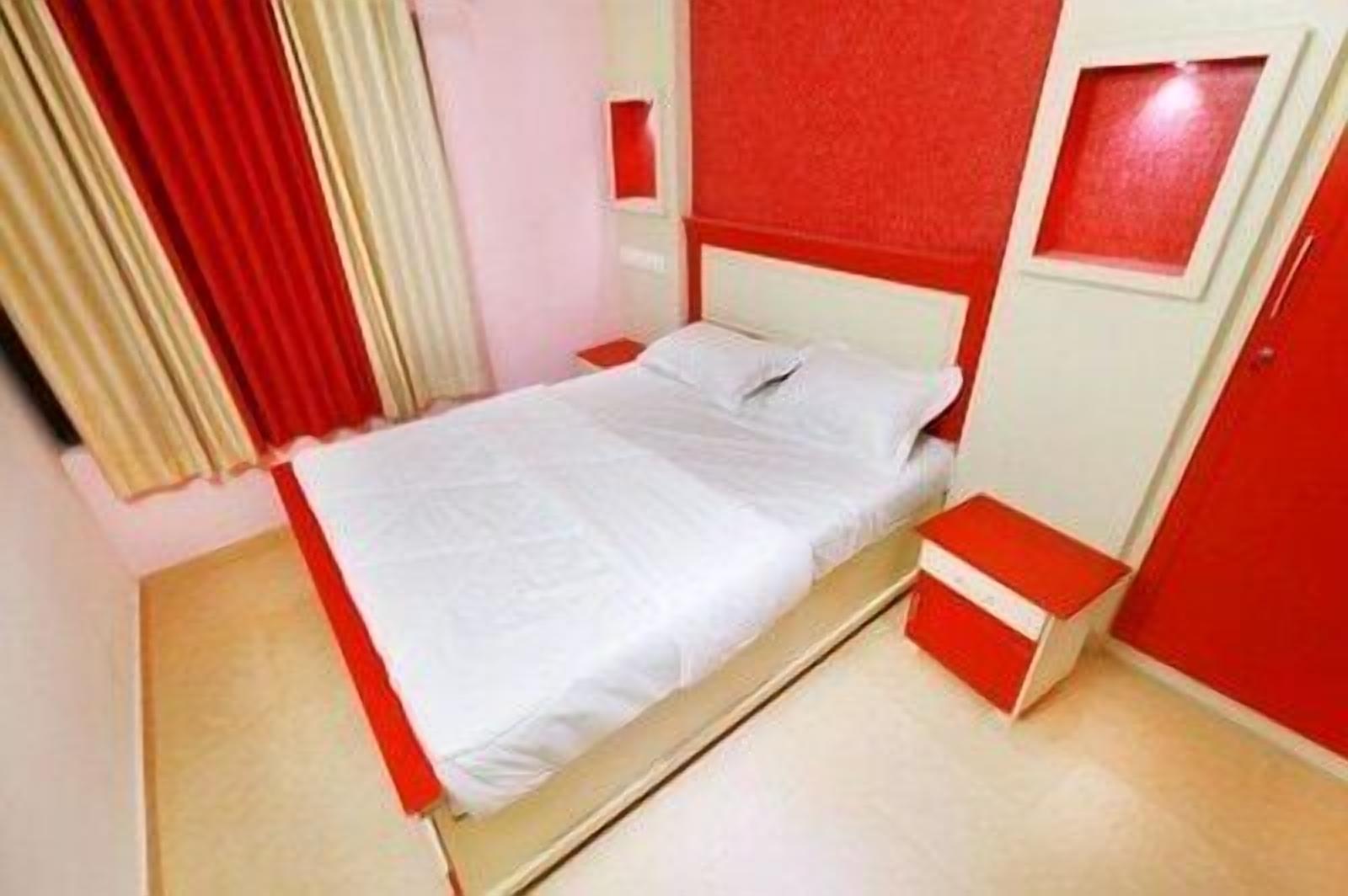 A bed with white bedding in a room with red walls and a red door.
