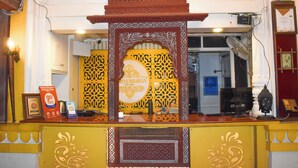 A reception desk with a traditional design, a framed sign, a fan, and a clock. - Shanti Bhawan Heritage Hotel (Jodhpur)