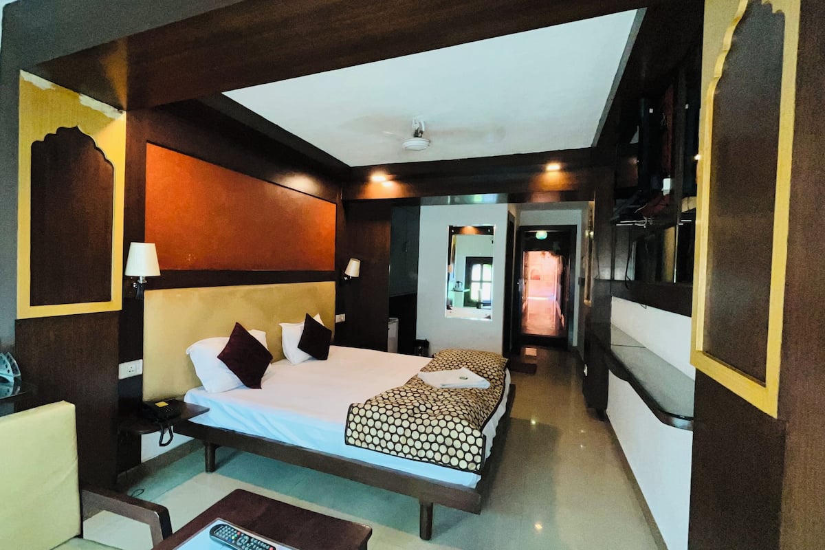A hotel room with a bed, bedside tables, a desk, a mirror, and a door leading to a bathroom.
