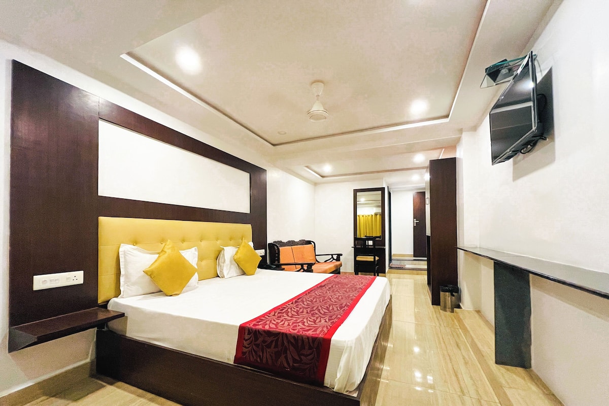 A hotel room with a bed, a television, a mirror, and a door leading to a bathroom.