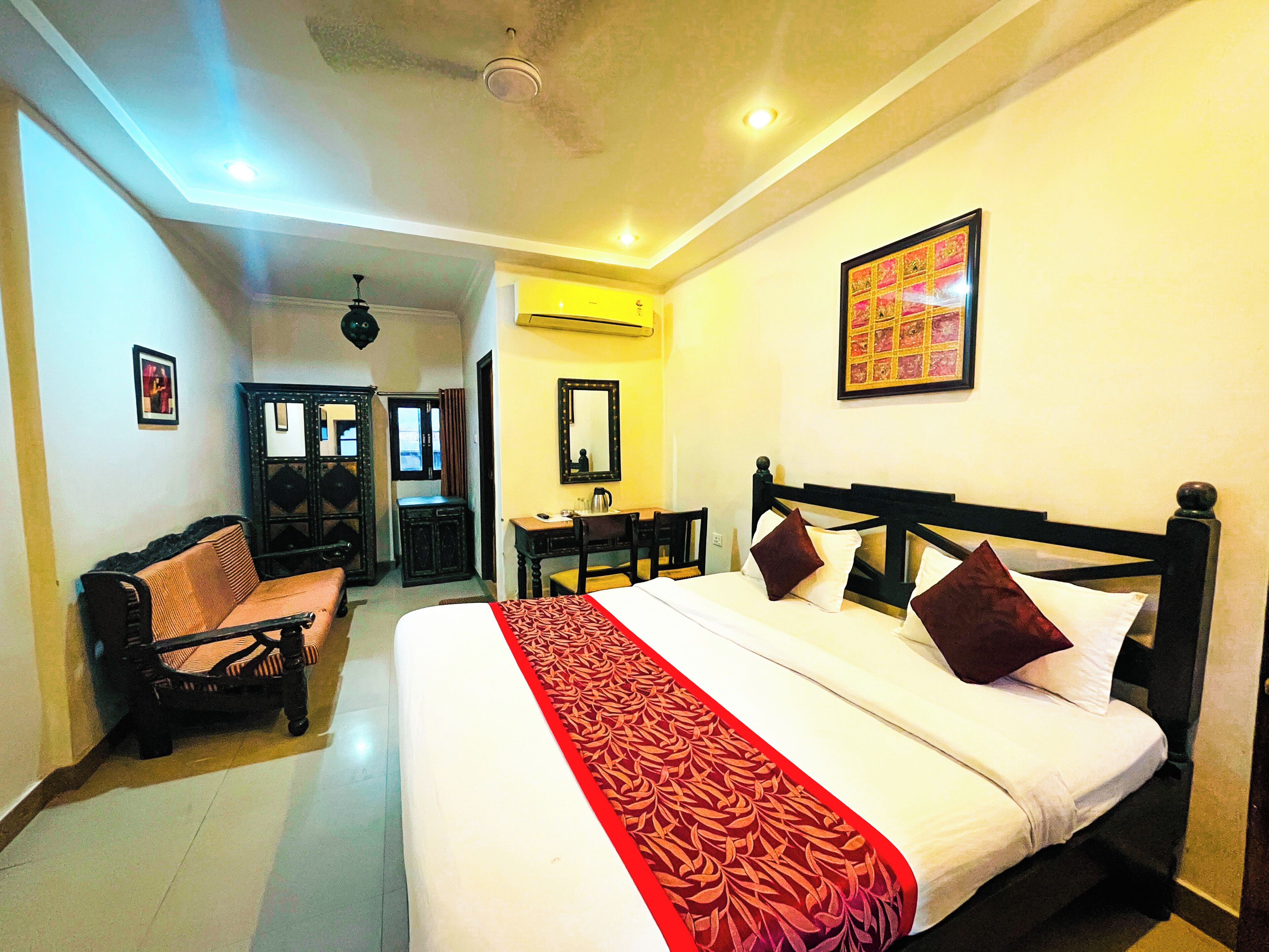 A hotel room with a large bed, a desk, a chair, a sofa, and a mirror.