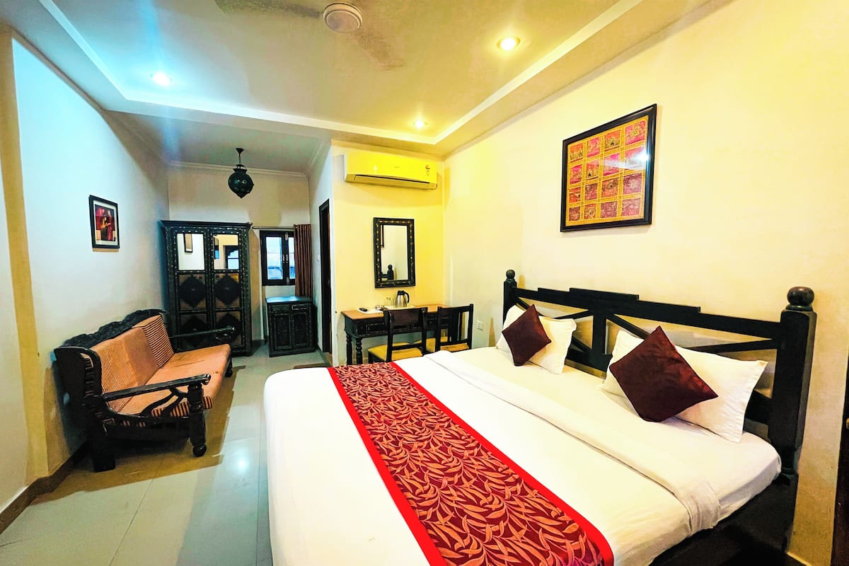 A hotel room with a large bed, a desk, a chair, a sofa, and a mirror.