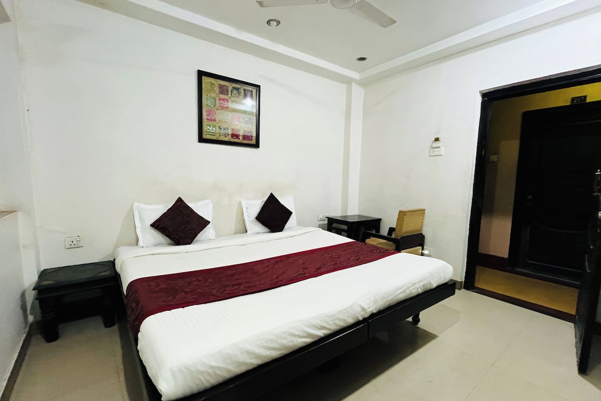 A hotel room with a bed, a ceiling fan, a framed picture on the wall, and a door.