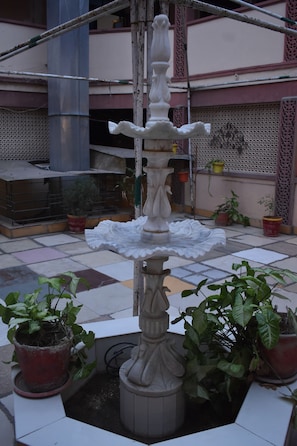 A fountain with multiple tiers and a base surrounded by potted plants.