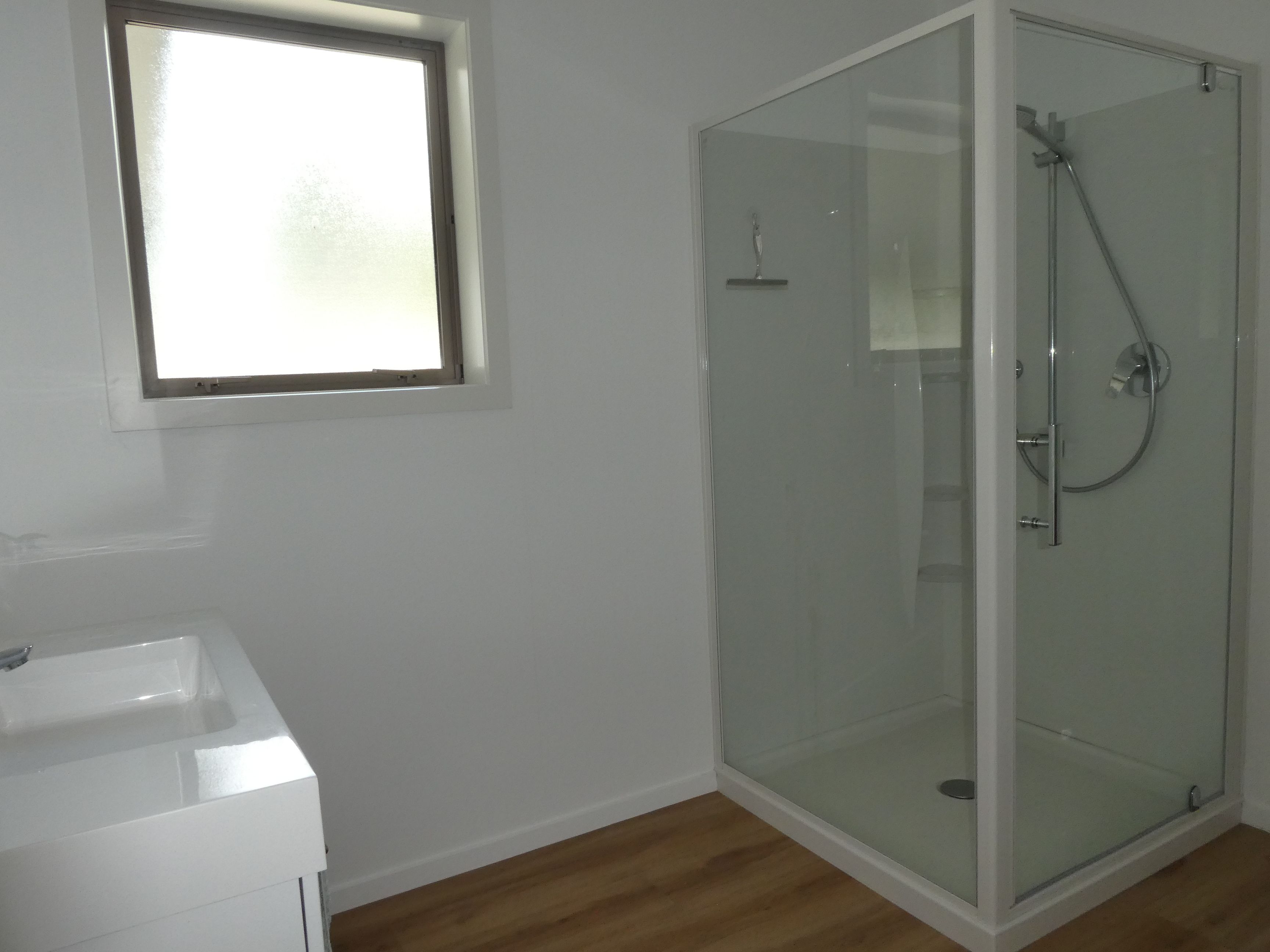 A bathroom with a glass shower enclosure, a white sink, and a window.