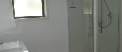 A bathroom with a glass shower enclosure, a white sink, and a window.