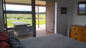 Un dormitorio con cama, cómoda de madera y puerta corrediza de vidrio que da a un patio exterior con mesa y sillas.