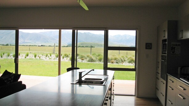 Una cocina moderna con una isla grande, un comedor y vistas a un campo de césped y monta ñas a través de amplios ventanales.