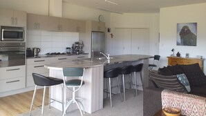 Una cocina moderna con una isla central, taburetes de bar y un área de comedor con sofá y cojines.