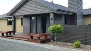 A modern house with a grey exterior, a chimney, and a small front yard with a bench and a potted plant. - Glencairn Beauty (Twizel)