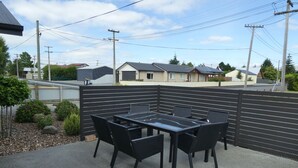 An outdoor patio with a glass-top table and black chairs, surrounded by a black fence. - Glencairn Beauty (Twizel)