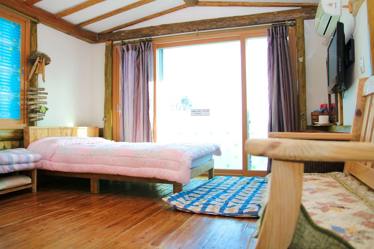 Una habitación con una cama de madera, una mesita de noche pequeña, una ventana con cortinas y un techo de madera.