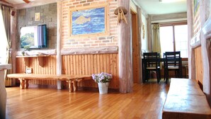 Interior de madeira com parede de tijolos, um banco de madeira, uma mesa e um vaso com planta.