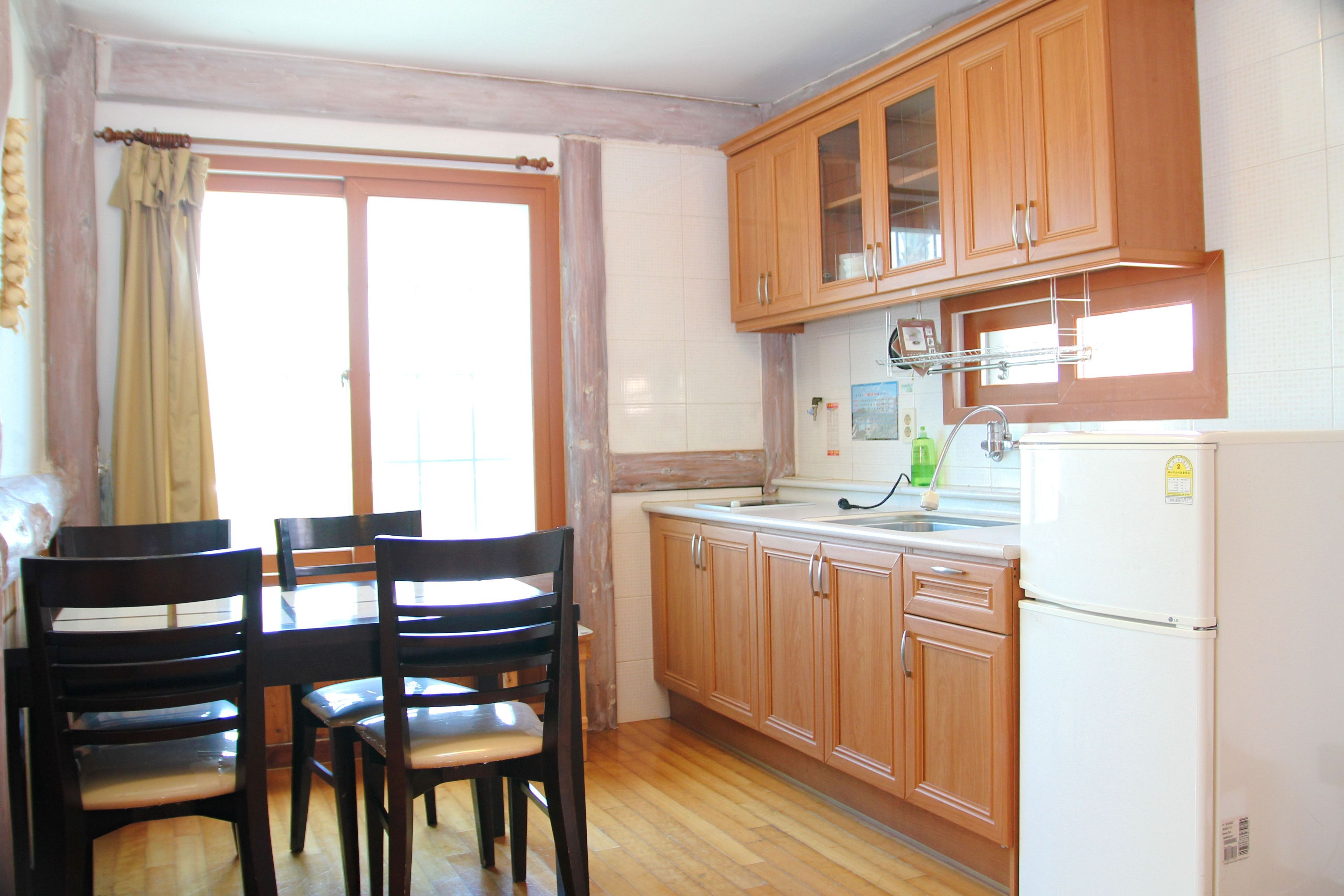 A kitchen with wooden cabinets, a refrigerator, a sink, and a dining table with chairs.
