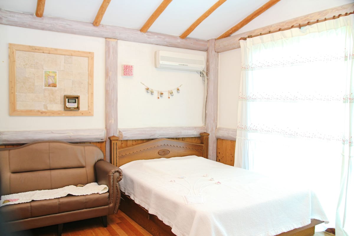 Un dormitorio con cama de cabecera de madera, sofá de cuero marrón y aire acondicionado instalado en la pared.