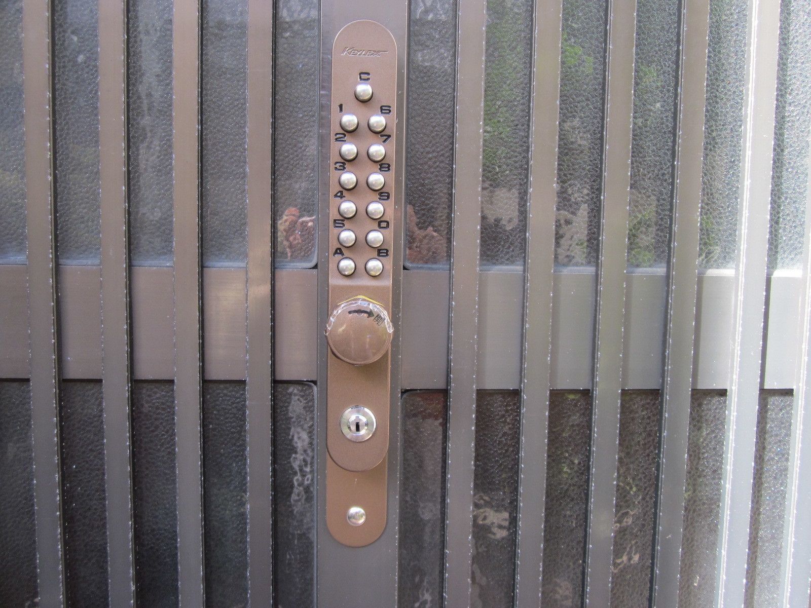 A keypad lock on a metallic surface with vertical bars.