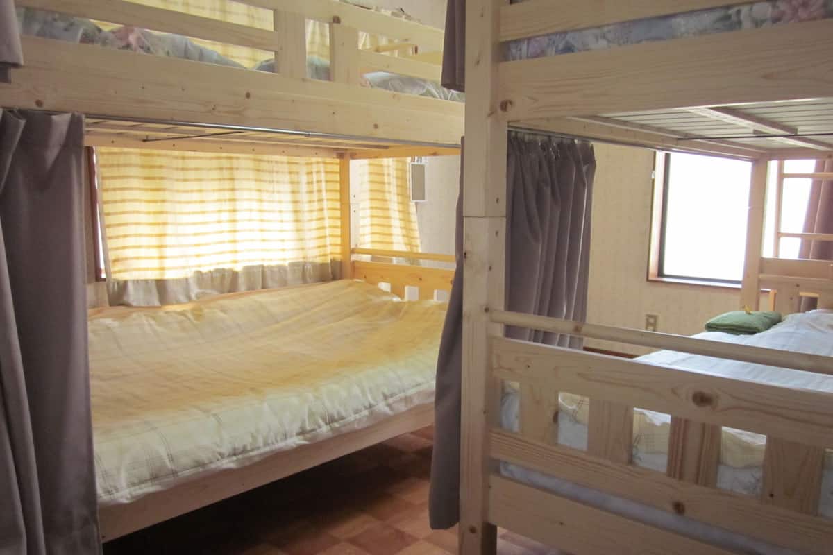 Quarto com beliches, piso xadrez, camas de madeira e janela com cortinas.