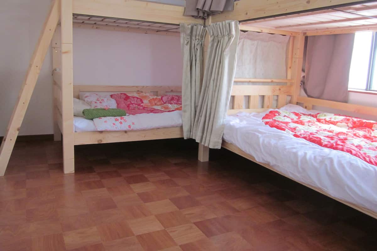 Quarto com beliches de madeira, soalho xadrez de madeira e janela com cortinas.