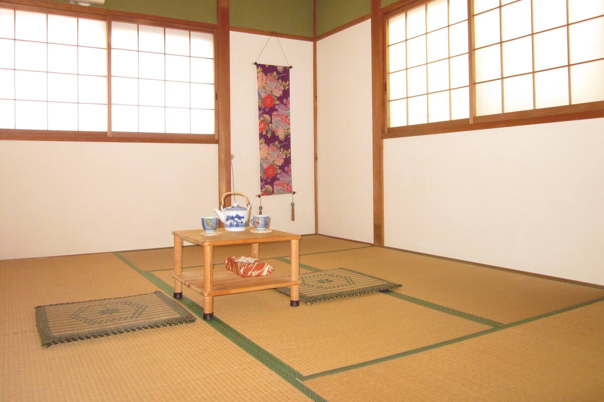 Um espaço com esteiras de tatame, uma mesa de tatame, um pergaminho pendurado e um conjunto tradicional de chá japonês.