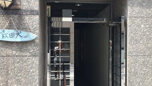 A building entrance with a metal sign, a wooden bench, and a glass door. - bnb+ Akihabara - Hostel, Caters to Women (Tokyo)