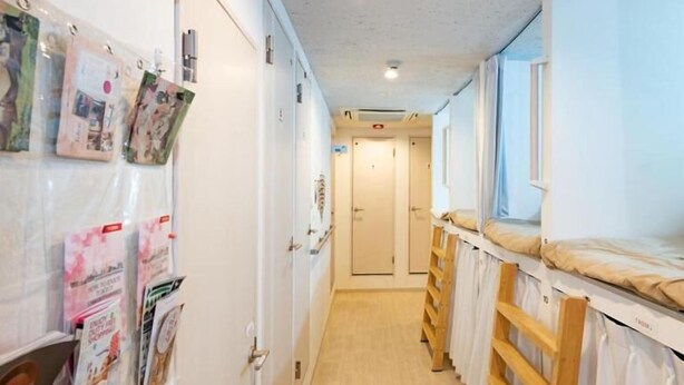 A corridor with bunk beds, a bulletin board with photos, and a door at the end. - bnb+ Akihabara - Hostel, Caters to Women (Tokyo)