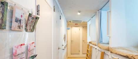 A corridor with bunk beds, a bulletin board with photos, and a door at the end.