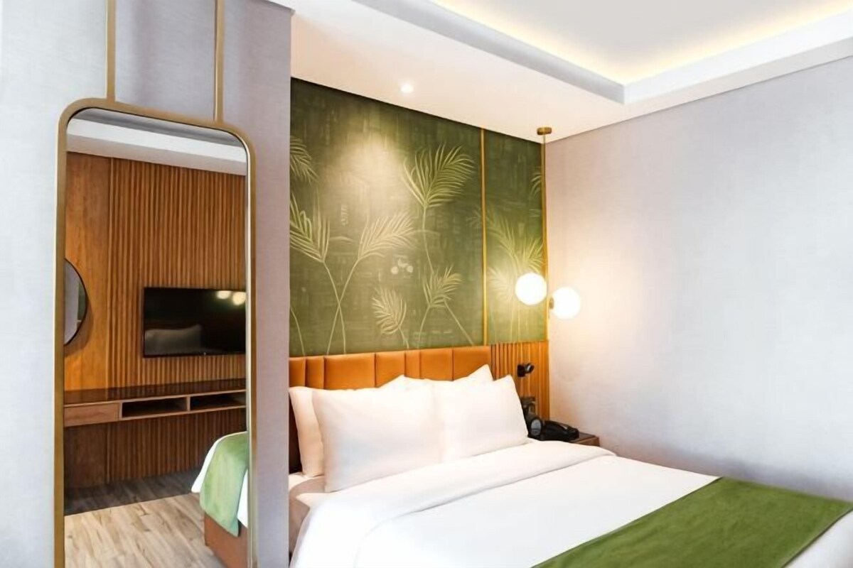 A modern hotel room with a bed, a television, a wall-mounted TV, and a green decorative panel.