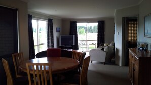Een kamer met een eettafel, stoelen, een televisie, een bank en een keukenhoek.