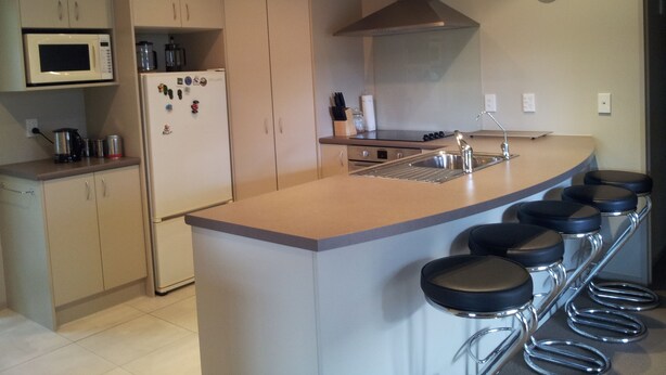 Een moderne keuken met een centraal eiland, barkrukken, een magnetron en een koelkast.