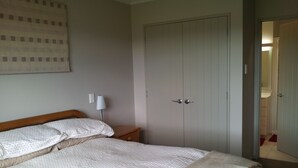 Een slaapkamer met een bed, nachtkastje, lamp en een kledingkast.