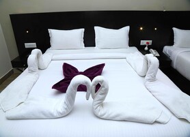 Een hotelkamer met een net opgemaakt bed, witte handdoeken gevouwen in de vorm van een zwaan, een kussen met een paarse strik en een zwart hoofdeinde.