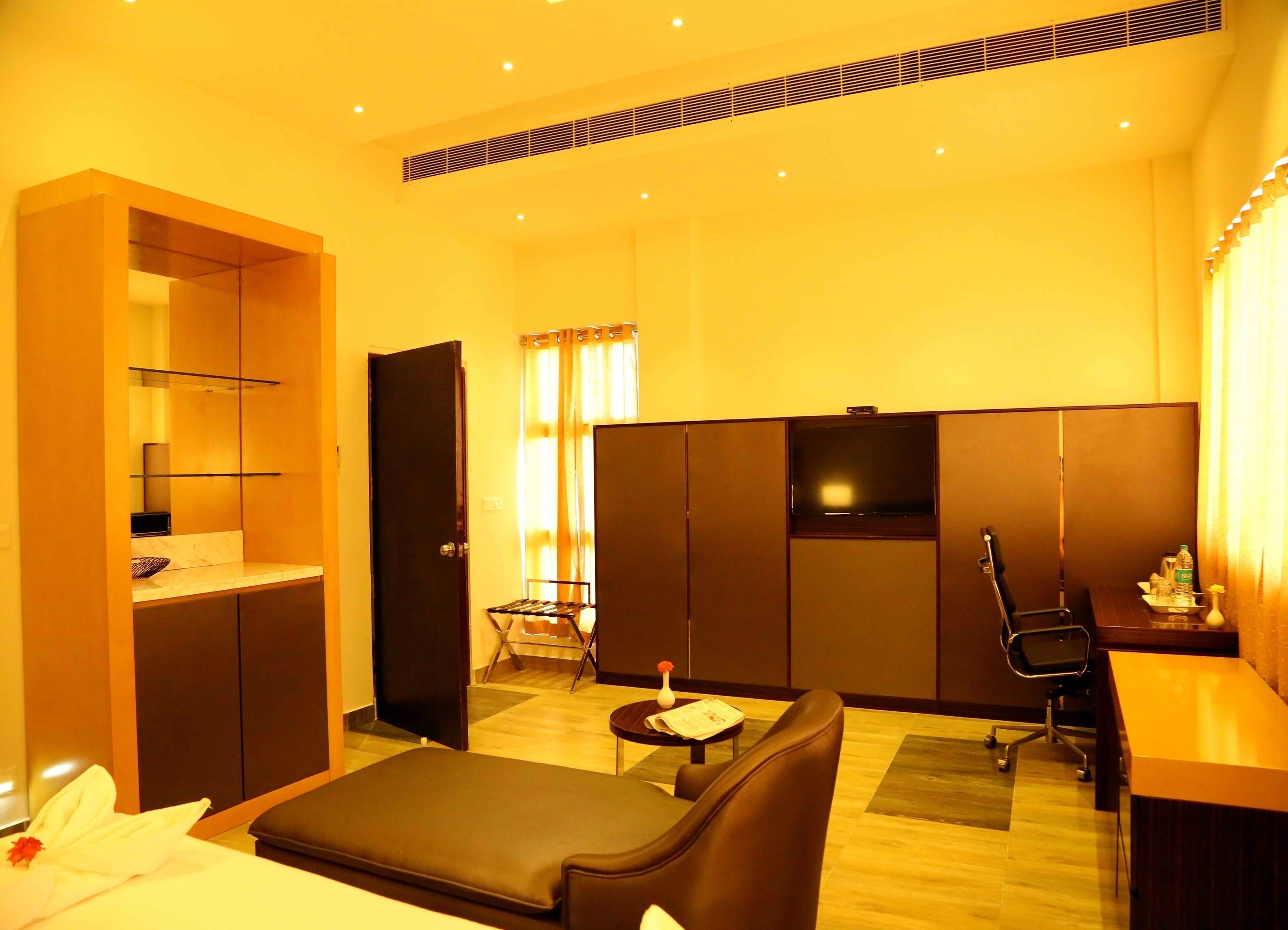 A hotel room with a bed, a desk, a chair, a small table, a wardrobe, and a television.