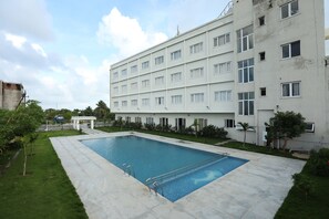 Piscina rectangular con una escalera metálica, rodeada de un área pavimentada, una valla blanca y palmeras.