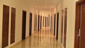 A long, well-lit hallway with wooden doors on both sides, leading to multiple rooms. - Queens Inn (Velankanni)