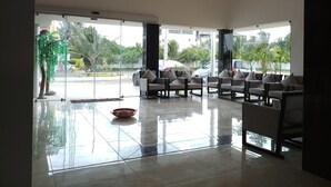 A spacious lobby with a modern design, featuring a seating area with multiple chairs and a reflective tiled floor. - Queens Inn (Velankanni)