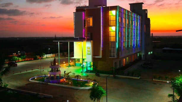 A hotel with a prominent sign, a well-lit entrance, and a landscaped area with a fountain. - Queens Inn (Velankanni)
