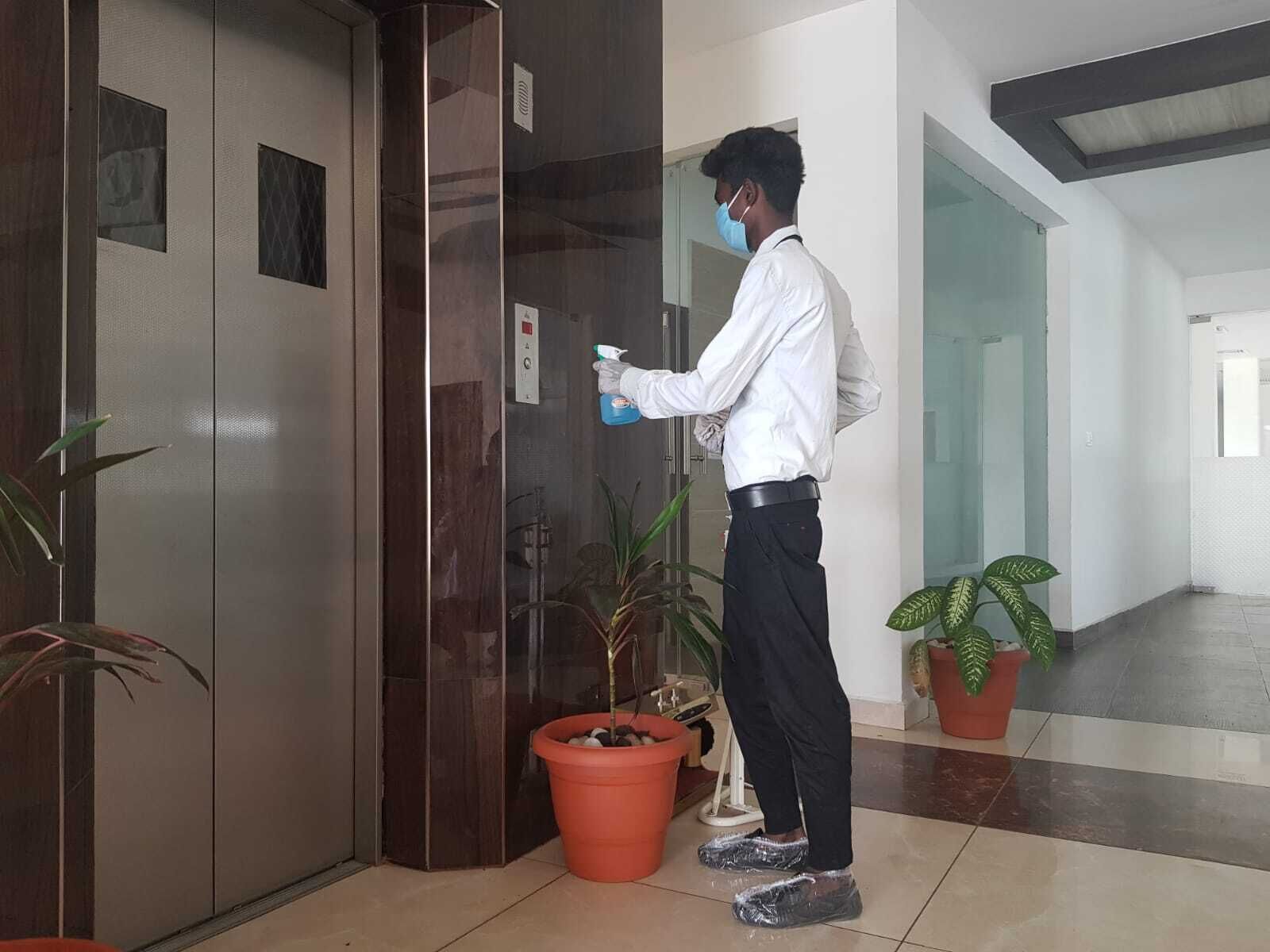Una persona limpiando un picaporte en un pasillo con plantas en macetas y suelo de baldosas.