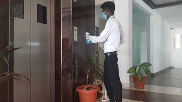 Una persona limpiando un picaporte en un pasillo con plantas en macetas y suelo de baldosas.
