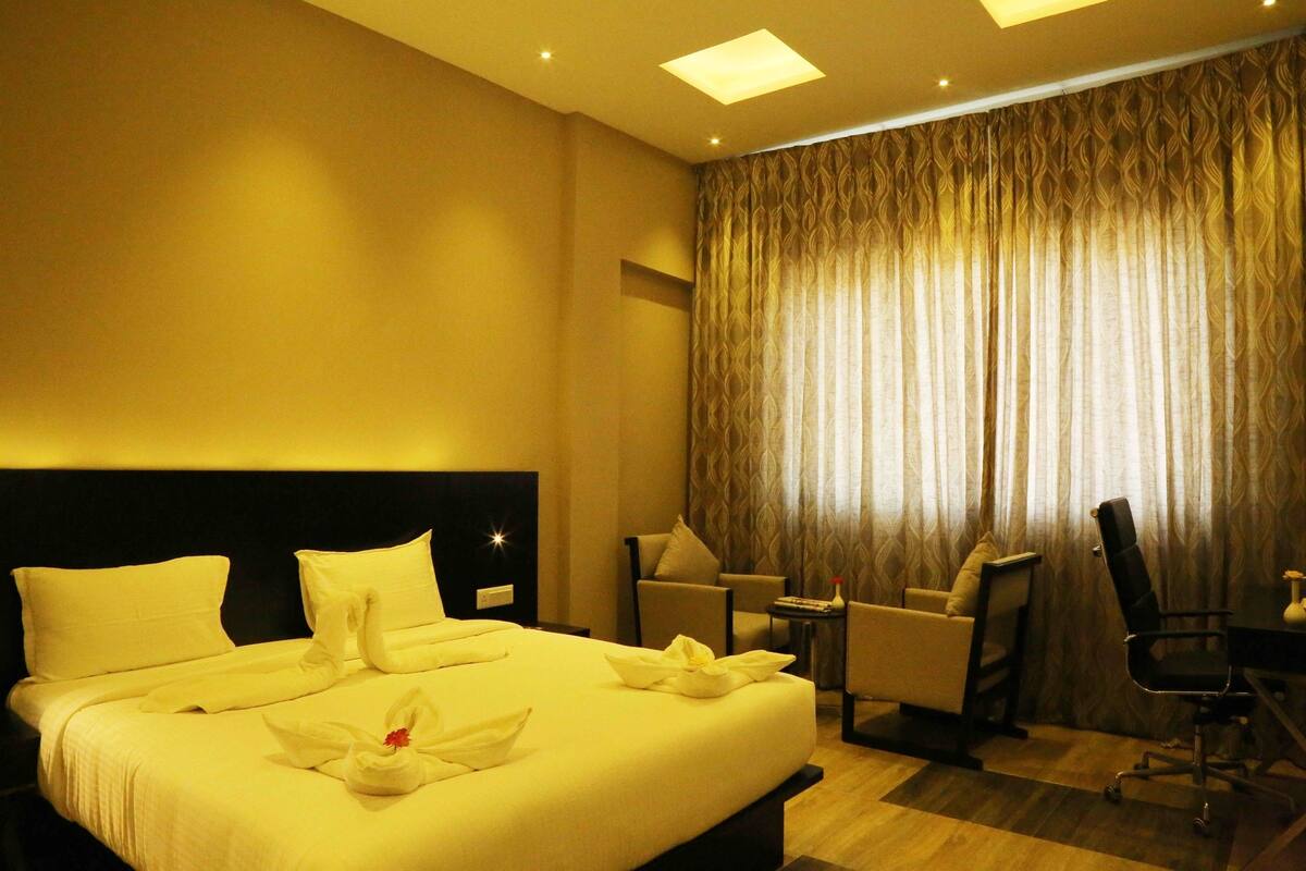Une chambre d’hôtel avec un grand lit, un bureau, deux chaises et un rideau.