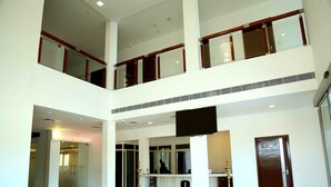 A multi-level hotel lobby with a reception desk, a staircase, and a decorative lamp. - Queens Inn (Velankanni)