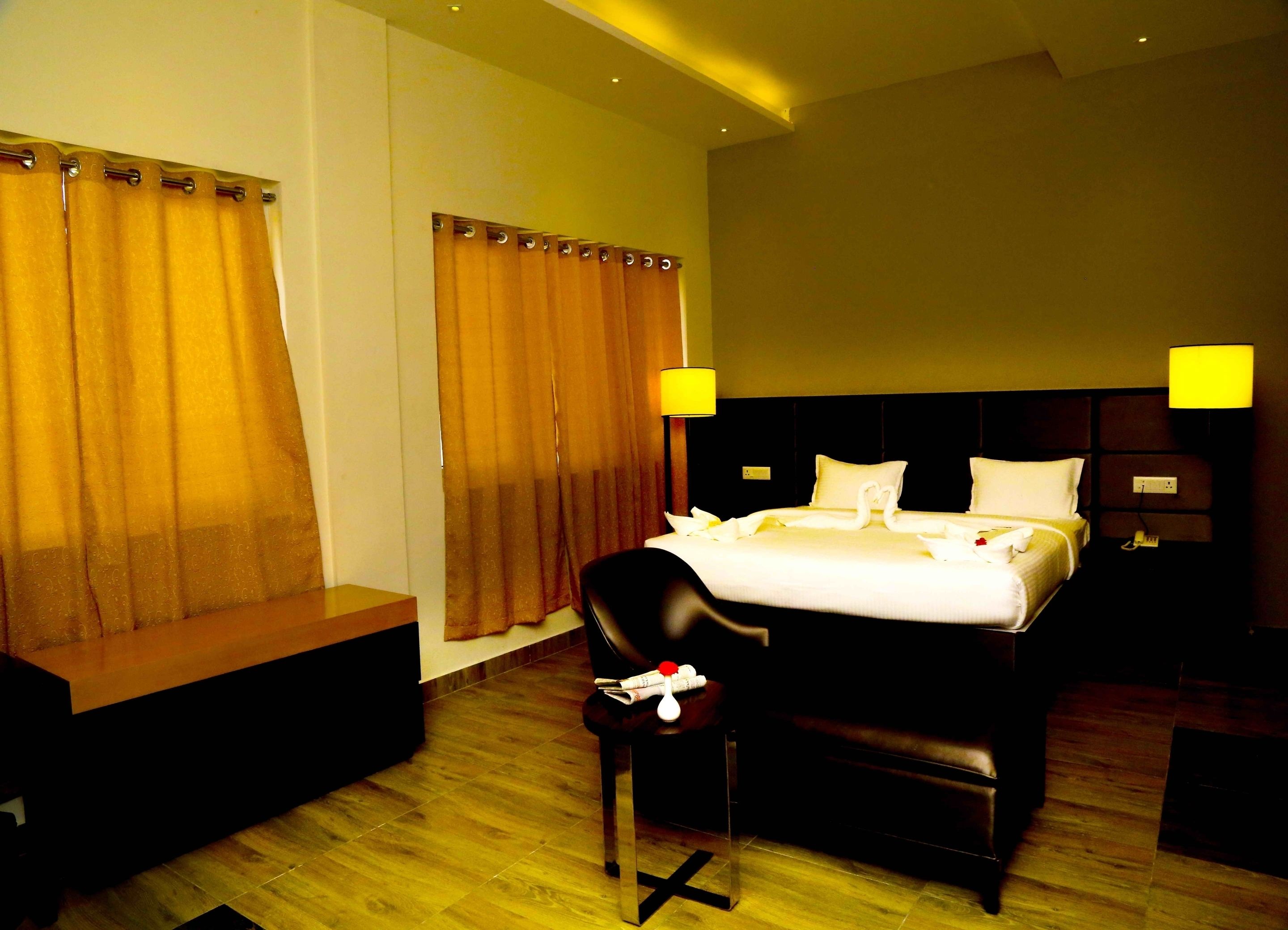 A hotel room with a large bed, two bedside lamps, a wooden headboard, a bench, and a chair.