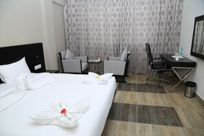 Una habitación de hotel con una cama bien hecha, dos sillones, un escritorio y un cubo de basura.